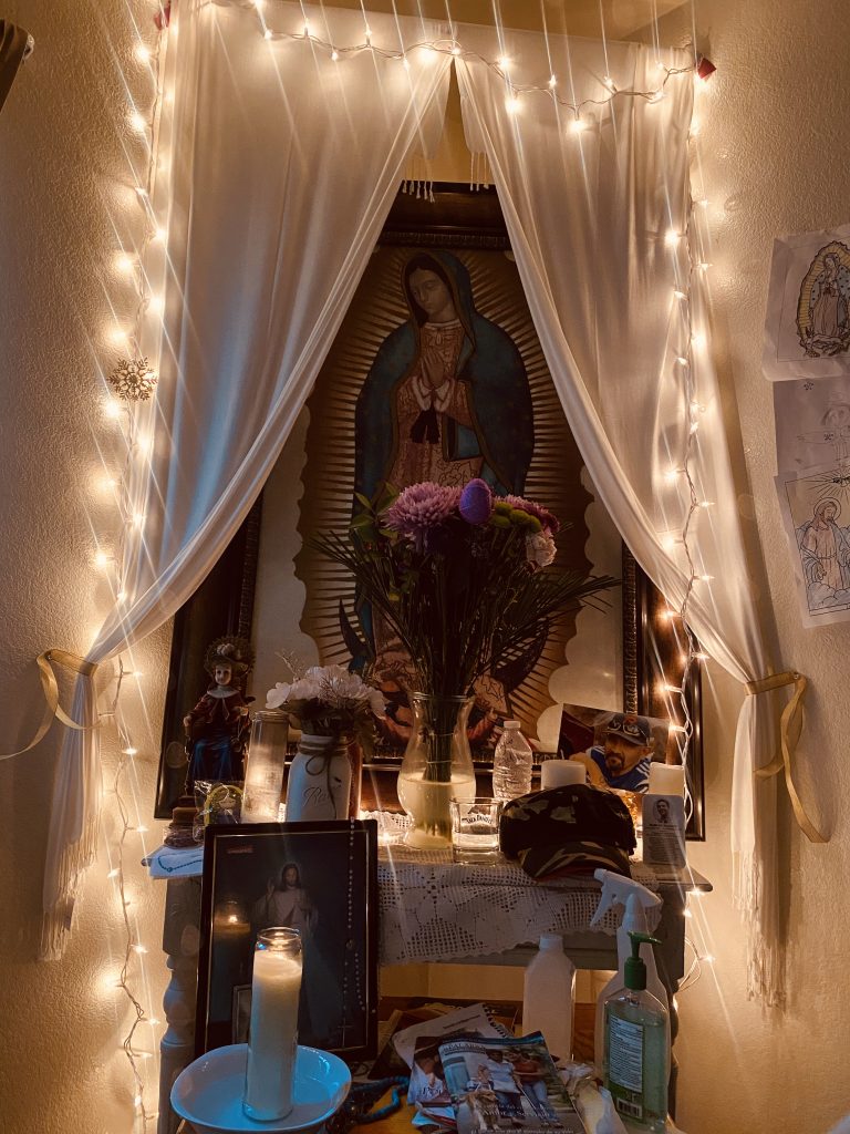 Cristina Hernandez (Chico, CA),	"La virgencita	".  I specifically chose this altar to photograph because I remember during holidays or after mass family and friends would come and pray the rosary together. After prayer we would sit together having hot chocolate or tea with cookies talking and enjoying each other’s company. Now it has become a corner of peace and silence for me. Whether it is one hour or five minutes where I am on my knees praying before work this corner has relieved me of panic, fear, and anxiety about what is going on around the world. I miss the times when everyone was around this corner, but now it has become a corner of my house I spend some of my spare time finding comfort and peace and I am grateful for this beautiful corner.