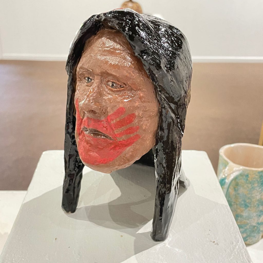 Lucky Preston, "Missing and Murdered Indigenous Women", 2021, Ceramic and mixed media.

These pieces carry the red handprint over the mouths to draw attention to the “Silent-No-More” of the Missing and Murdered Indigenous Women Movement.
For decades throughout the world, thousands of Indigenous women and girls have disappeared without a trace and without follow-up by the authorities, leaving families heartbroken. 
The Red-Hand icon serves to bring awareness to the issue. Recently, President Biden declared May 5th as Murdered and Missing Indigenous Women Awareness Day.